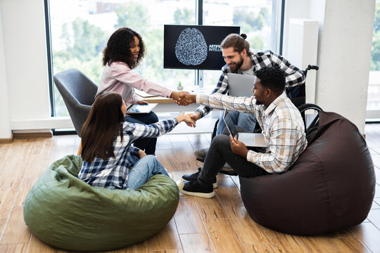 Group of diverse coworkers in modern setting shake hands, collaborating on artificial intelligence development project, symbolizing teamwork, innovation, and successful accomplishment