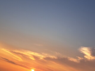 Obraz premium Evening sunset with an orange blue sky – White and grey clouds illuminated by the last remaining rays of the bright orange evening sun, amidst a darkening blue sky.