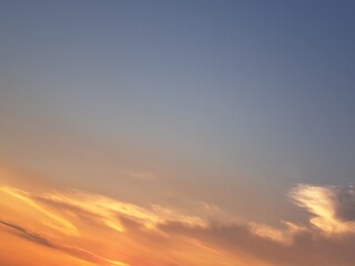 Evening sunset with an orange blue sky – White and grey clouds illuminated by the last remaining rays of the bright orange evening sun, amidst a darkening blue sky.