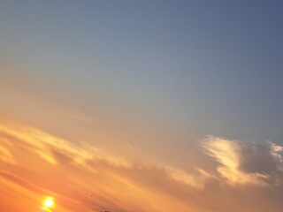Fototapeta premium Evening sunset with an orange blue sky – White and grey clouds illuminated by the last remaining rays of the bright orange evening sun, amidst a darkening blue sky.