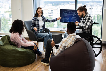 Group of young adults including woman in wheelchair discussing car blueprint design ideas collaboratively in modern office setting. Focus on teamwork inclusivity creativity innovation auto engineering