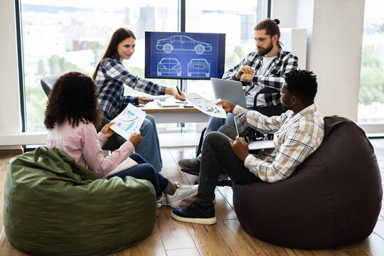 Young diverse adults discussing car design concepts in office using documents and screens. Collaborative effort with focus on teamwork and innovative solutions for engineering and construction tasks - Powered by Adobe