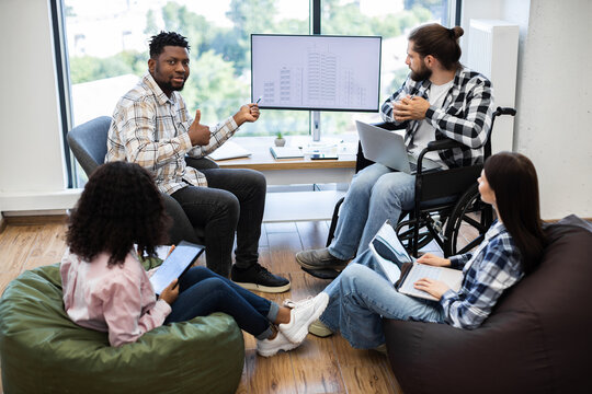 Diverse group of colleagues brainstorming together on architectural project using laptops and plans. Inclusive workplace featuring individuals of different races, genders, and abilities contributing