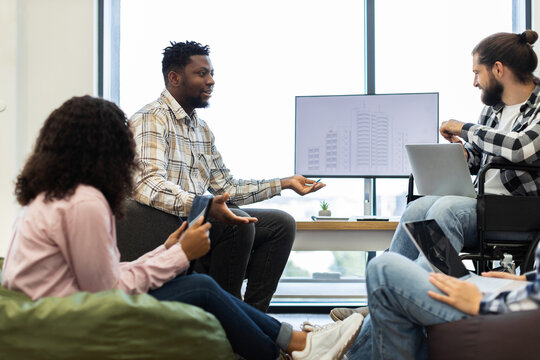 Diverse group of colleagues collaborating on project in office environment. Three adults of different races and genders, mid twenties to early thirties, using technology for discussion.