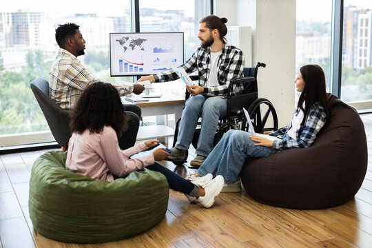 Group of four people, diverse backgrounds, discussing finances and strategies in modern, relaxed workspace with charts