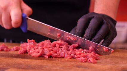 Butcher grinding fresh beef meat in a professional meat grinder inside butcher shop