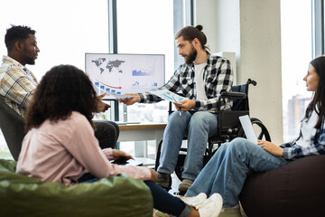 Professionally dressed coworkers discussing financial data around office table. Image features diverse individuals, including male in wheelchair and three colleagues.