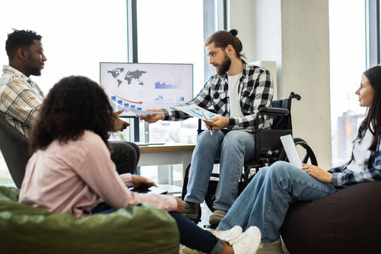 Professionally dressed coworkers discussing financial data around office table. Image features diverse individuals, including male in wheelchair and three colleagues.