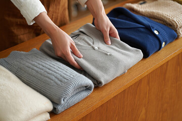 Hands organizing folded sweaters on wooden dresser in cozy interior 
