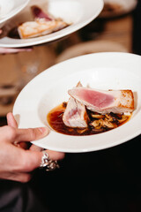 Gourmet dish with seared tuna served in broth.Close-up of a gourmet dish featuring seared tuna fillet served over vegetables and mushrooms in a savory broth, held by a waiter.