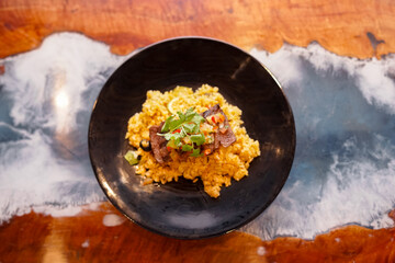 A serving of Asian-style fried rice on a black plate, topped with grilled beef slices, fresh coriander, chopped vegetables, and a slice of lime.
