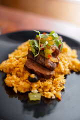 A serving of Asian-style fried rice on a black plate, topped with grilled beef slices, fresh coriander, chopped vegetables, and a slice of lime.