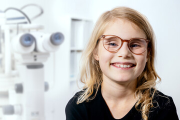 smiling little girl with eyeglasses after eyesight test visit at ophthalmologist office. eye health and correction