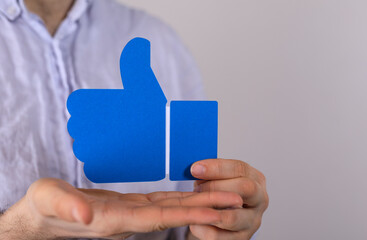 Image of a hand holding a blue thumbs up symbol, representing approval, like, positive feedback, and success.