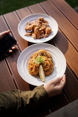 Two plates of fried chicken dishes served on wooden table, Asian style cuisine with garnish and lemon slice.