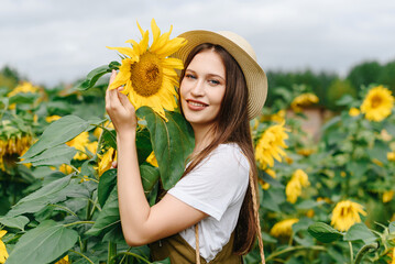 young beautiful brunette caucasian woman on farm in sunflower field in summer day, smiling widely, eco style clothes, green dress, straw hat