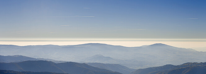 A panoramic view of layered mountain ridges bathed in soft light, creating a serene and tranquil natural landscape.