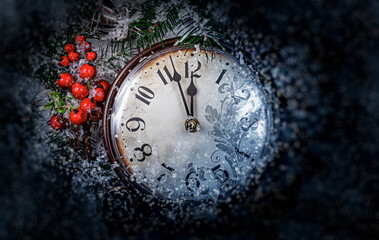 A vintage clock decorated with red berries and pine branches is covered in frost and snow, showing midnight as a festive symbol of New Year Eve celebration.