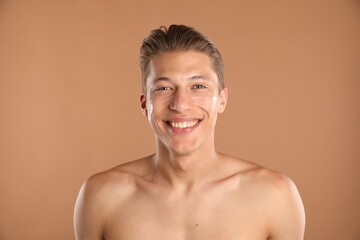 Handsome young man with cream on his face against light brown background