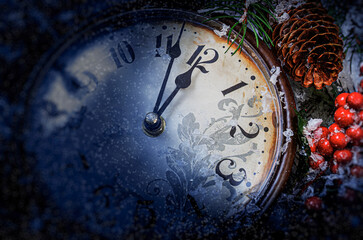 A vintage clock decorated with red berries and pine branches is covered in frost and snow, showing midnight as a festive symbol of New Year Eve celebration.