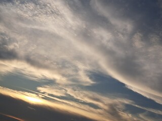 Evening sunset with a yellow blue sky – White and grey clouds illuminated by the last remaining rays of the bright yellow evening sun, amidst a darkening blue sky.