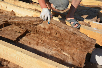A builder checks the correctly laid layers of basalt rock wool thermal insulation on the roof.Basalt rock wool insulation is a mineral wool product made by melting natural basalt rock.