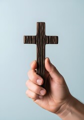 Hand holding a wooden cross against a light blue background