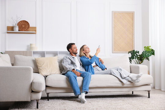 Couple using remote to control air conditioner on sofa at home