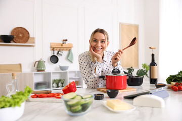 Portrait of smiling woman with spoon cooking at table in kitchen