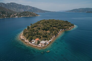 Drone aerial view of a lush islet situated on a tiny peninsula featuring a historic school building in a coastal town