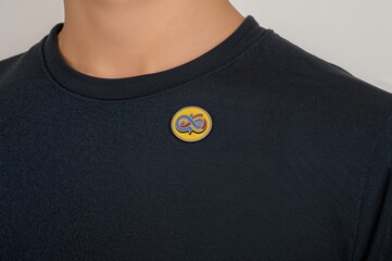A young boy wears a shiny pin with the rainbow infinity emblem on his shirt to show his backing of autism advocacy on a special awareness day