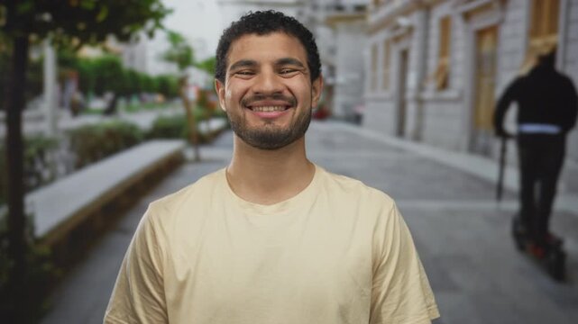 Man puckers lips on sunlit street with building facades, rows of stone benches, and leafy trees under soft afternoon light; playfulness.