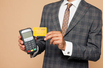 Close up young employee business man corporate lawyer he wears formal grey suit shirt tie work in office hold bank payment terminal to process acquire credit card isolated on plain beige background.