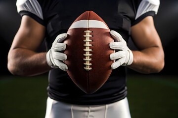 Close-up of football player in black jersey holding ball with both hands, focused and ready under dramatic lighting in intense game atmosphere