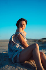 A girl in a gray dress walks on a sand dune at sunset in summer