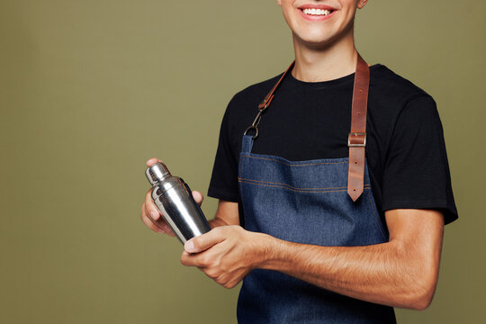 Cropped young man barista bartender barman employee wear jeans apron t-shirt work in night club hold shaker for preparing cocktails isolated on plain green background. Small business startup concept.