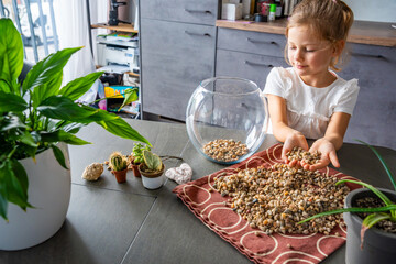 Little girl pouring stones into glass container to create drainage for future florarium or closed ecosystem. Hands-on learning, eco-friendly creativity and early involvement in nature-based projects.