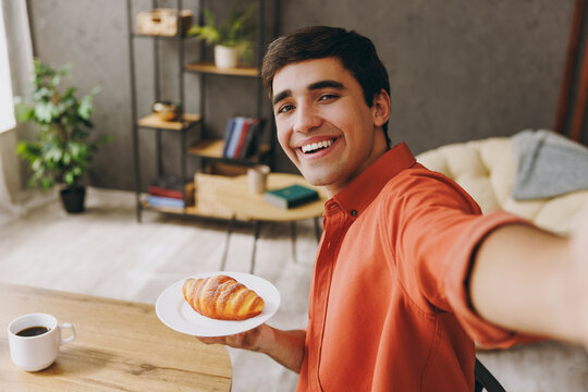 Close up young man wear casual clothes eat croissant do selfie shot on mobile cell phone sit alone at table in coffee shop cafe relax rest in restaurant in free time indoors. Freelance office concept.