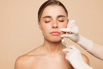 Beautiful half naked topless young woman 20s with nude make up getting lip beauty injection isolated on plain beige color background studio portrait. Skin care healthcare cosmetic procedures concept.
