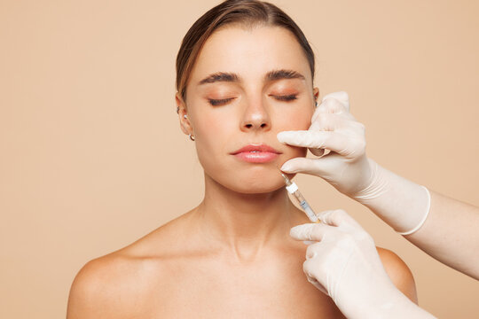 Beautiful half naked topless young woman 20s with nude make up getting lip beauty injection isolated on plain beige color background studio portrait. Skin care healthcare cosmetic procedures concept.