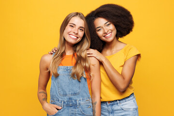 Two young happy cheerful friends buddies women they wear denim casual clothes hug together look camera with toothy smile isolated on plain yellow orange background studio portrait. Lifestyle concept.