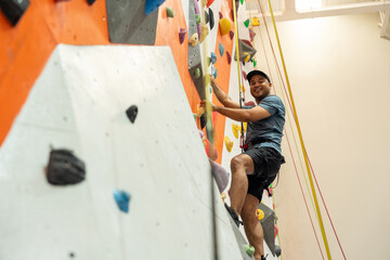 Excited moment Confident man enjoys indoor climbing as part of his urban fitness lifestyle. Asian male embracing rock climbing adventure sport workouts popular among the new generation.