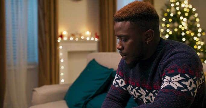 An upset young man sits on a couch. After a call with his boss, he learned he was fired, so he threw the phone aside and put his hand to his head in frustration.