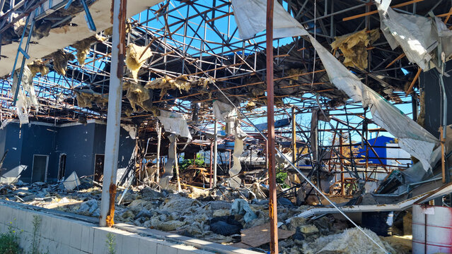 Destroyed industrial building with collapsed roof and exposed metal framework. Piles of insulation material and debris on the ground. Explosion damage