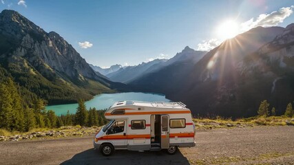 Tilting camera upward as sun peeking behind ridge, showing orange camper van on gravel overlook - Powered by Adobe