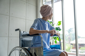 A cancer patient sits in a wheelchair with an IV drip looking stressed and sad. Asian Woman receiving IV therapy in a wheelchair showing visible signs of stress and depression