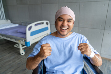 A male cancer patient in a wheelchair with an IV smiles with joy and hope showing strength and...