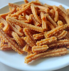 Close-up of homemade Murukku sticks in a white ceramic plate/White background/Still life