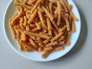 Close-up of homemade Murukku sticks in a white ceramic plate/White background/Still life