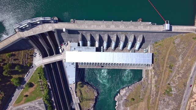 Aerial drone ascends in reverse over Roxburgh Dam, gradually unzooming to showcase the hydroelectric power station, reservoir, and surrounding Central Otago landscape.